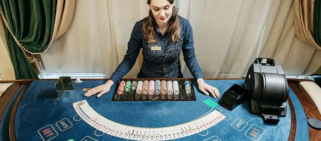 Az osztó ül egy kártyákkal és zsetonokkal megterített baccarat asztalnál.