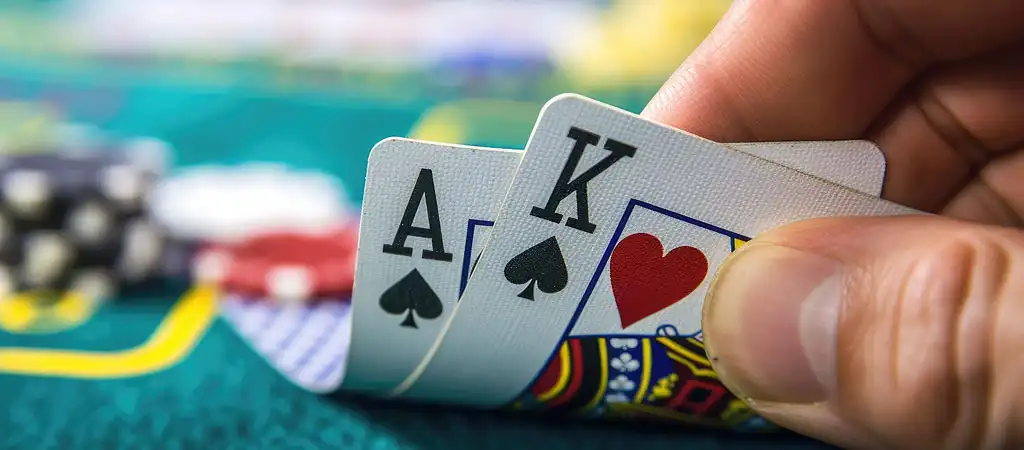 A játékos fekete ászt és királyt tart, amelyek a blackjack győztes kombinációját mutatják egy kaszinó asztalnál.