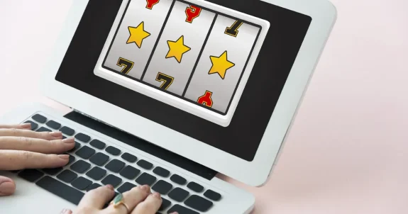 Laptopon futó online kaszinójáték nyerő szimbólumokkal, billentyűzeten játszó felhasználóval